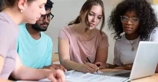 Grupo de jovens estudando finanças com livros e laptops.