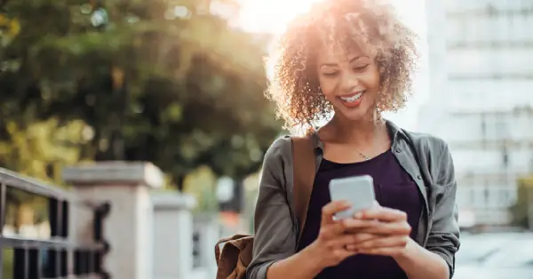 Mulher sorridente gerenciando sua conta internacional pelo celular.